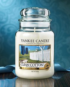 a yankee candle sitting on top of a wooden table next to a blue wall and fence