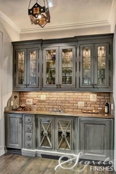 an old fashioned kitchen with grey cabinets and wood flooring in the center, along with a chandelier hanging from the ceiling