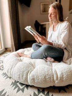 a woman is sitting on a bean bag chair reading a book in her living room