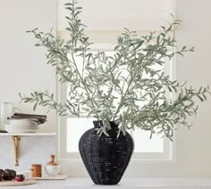 a black vase filled with green leaves sitting on top of a counter next to a window