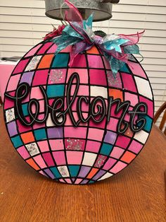 a pink and blue ball with the word welcome on it sitting on top of a wooden table