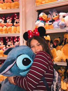 a woman is holding a stuffed animal in front of shelves full of mickey mouses