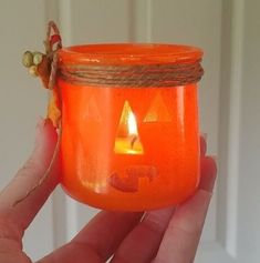 a hand holding an orange jar with a candle in it