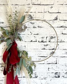 a wreath with red ribbon and greenery hanging on a brick wall in front of a white brick wall