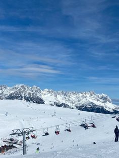 skiers and snowboarders at the bottom of a ski slope with mountains in the background