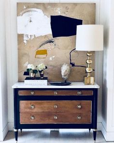 a black and white dresser with two lamps on it next to a large piece of art