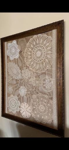 an old lace doily is hanging on the wall above a wooden framed artwork piece