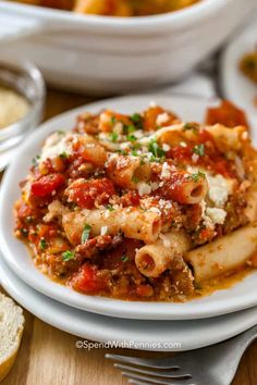 a white plate topped with pasta and meat covered in sauce on top of a wooden table