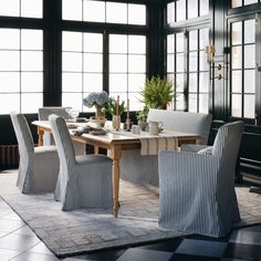 a dining room table and chairs in front of large windows with potted plants on them