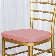 a gold chair with a pink seat pad on it's back and white curtain behind it