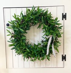 a wreath hanging on the front door of a house with white shutters and black handles