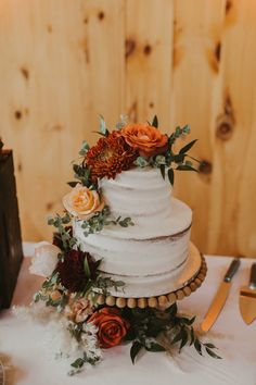 a white wedding cake with flowers and greenery sits on top of a wooden table