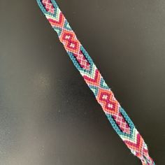 a close up of a colorful bracelet on a black surface with a red, white and blue bead