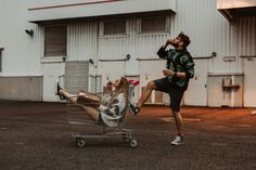 a man sitting in a shopping cart next to a woman laying on the ground with her legs up