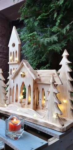 a small wooden church surrounded by trees with lights on it's sides and a candle in the center