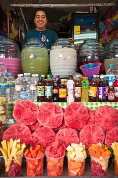 a man standing behind a counter filled with lots of fruit and vegetables next to water bottles