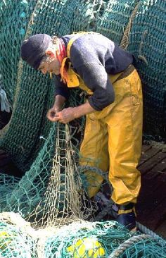 a man in yellow overalls standing next to some fishing nets