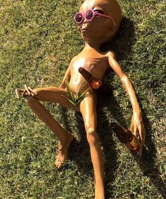 a doll laying in the grass with sunglasses on it's head and legs, wearing a pink sun glasses