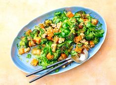 a blue plate topped with broccoli and tofu next to chopsticks