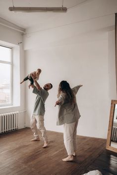 a man and woman holding a baby while standing in an empty room with a mirror