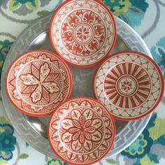 four red and white plates sitting on top of a silver plate covered in floral designs