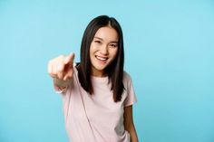 a woman pointing at the camera on a blue background with her hand in the air