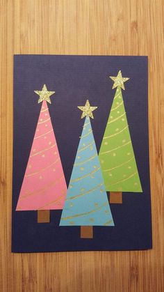 three christmas trees made out of construction paper on a wooden surface with gold glitter stars