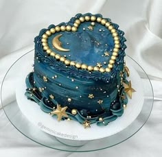 a blue cake with gold stars and a heart shaped decoration on the top is sitting on a glass plate