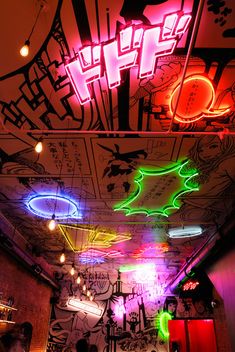 people are sitting in a brightly lit room with neon lights on the ceiling and graffiti all over the walls