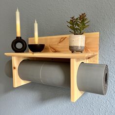 a wooden shelf with two candles and some other items on it next to a potted plant