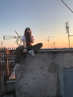 a young woman sitting on top of a cement wall talking on a cell phone while the sun is setting