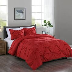 a bed with red comforter and pillows in a room next to a lamp on a table