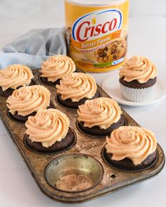 cupcakes with frosting in a muffin tin next to a can of bisco butter