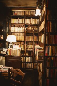 a room filled with lots of books next to a desk and lamp on top of it