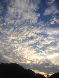 the sky is filled with clouds as the sun goes down in the distance behind some trees