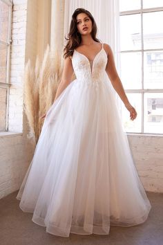 a woman in a white wedding dress standing by a window with her hands on her hips