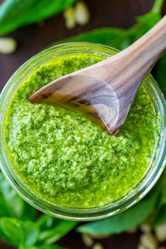 a wooden spoon in a jar filled with green pesto on top of some leaves