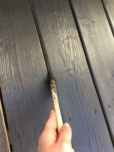 a person holding a paintbrush on top of a wooden floor next to a piece of wood