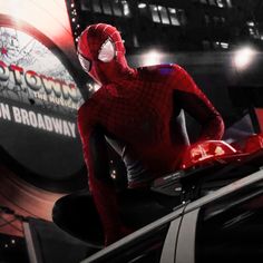 the amazing spider - man is sitting on top of his car