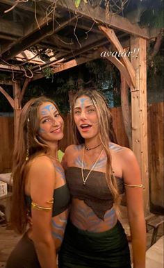 two beautiful young women standing next to each other in front of a wooden structure with vines on it