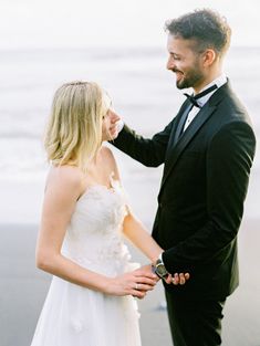 a man in a tuxedo and a woman in a wedding dress standing on the beach