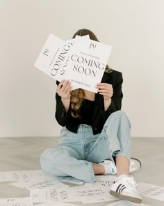 a woman sitting on the floor holding up two signs that read coming soon and coming soon