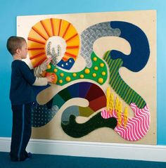 a little boy that is standing up in front of a wall with some art on it