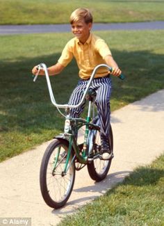 a young boy riding a bike down a sidewalk next to grass and trees in the background