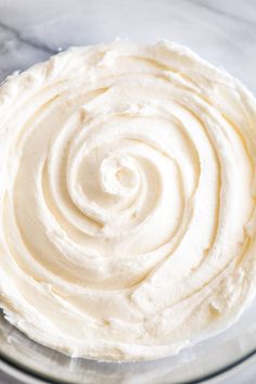 a glass bowl filled with white frosting on top of a marble countertop next to a knife