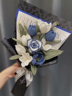 a crocheted flower bouquet is being held up by someone's hand in front of a greeting card