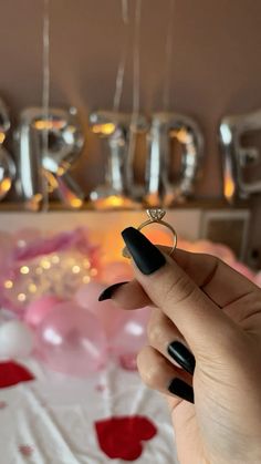 a woman's hand with black nail polish holding a ring