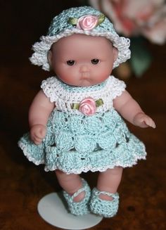 a small doll is wearing a blue dress and pink flowered hat with crocheted shoes