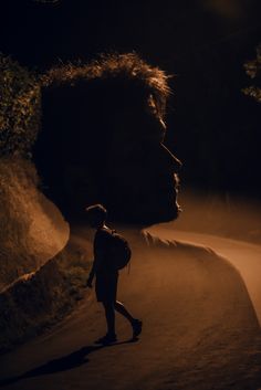 a person walking down a road at night with a large animal head in the background