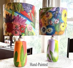 two lamps with flowers painted on them sitting on a table in front of a window